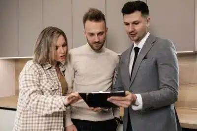 un couple et un agent immobilier regardent tous vers une tablette