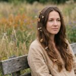 Femme aux cheveux ondulés ornés de fleurs séchées et d'épingles en bois dans une prairie naturelle