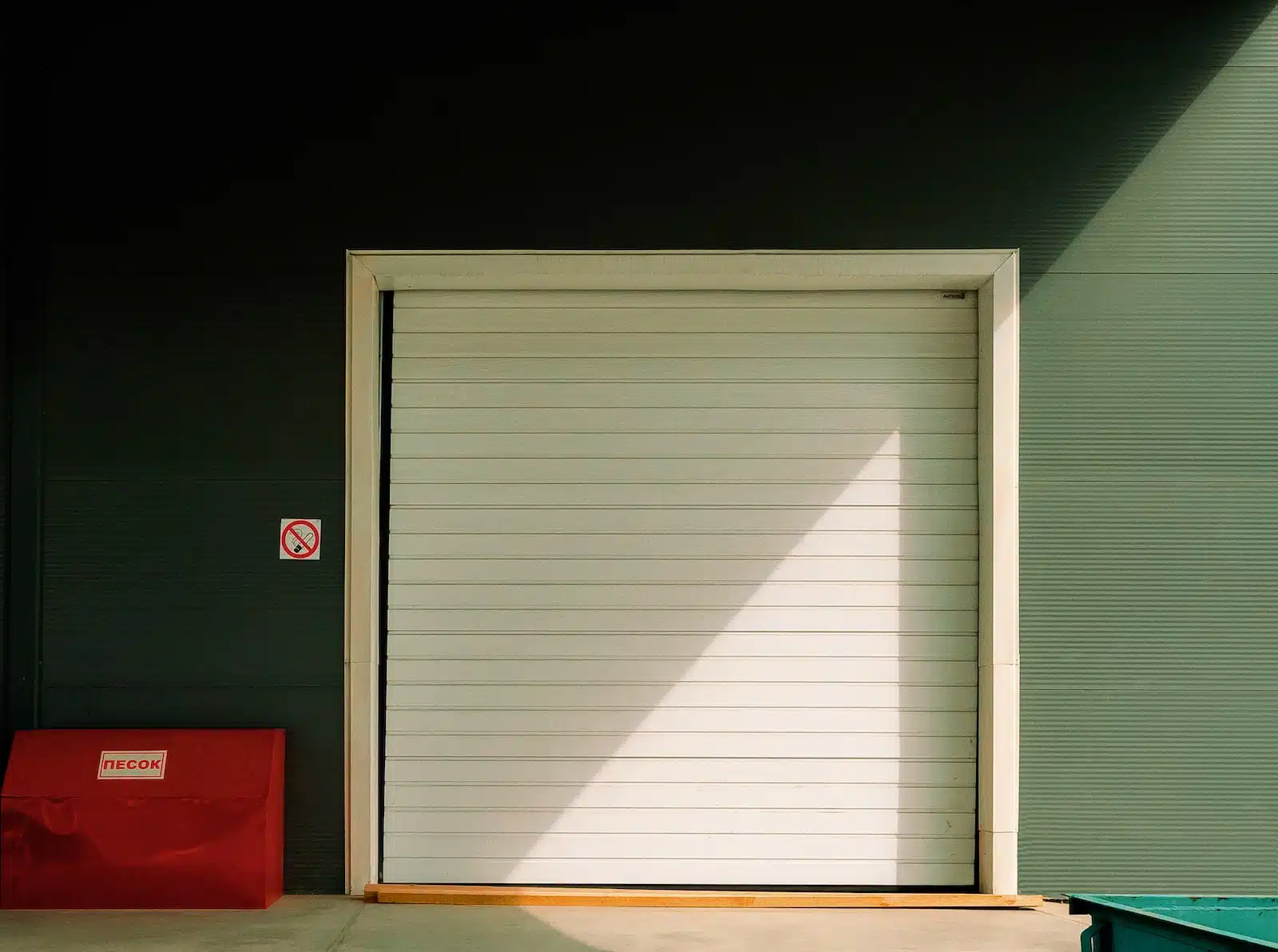 a closed garage door with a red trash can in front of it